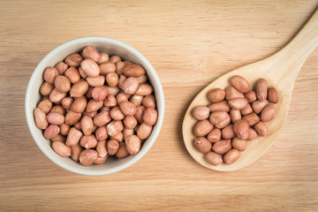 bowl of peanut and a scoop of peanut on a wooden background
