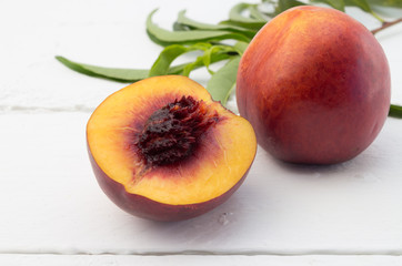 Close up photo of one ripe nectarine fruit and one cut in half on white wood background