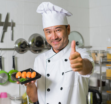 Asian chef sgowing plate with sushi and OK. Focus on sushi.