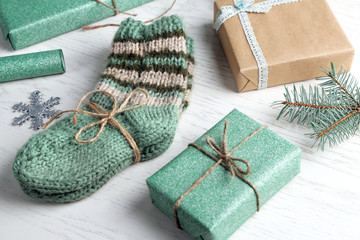 Pair of knitted socks with wrapped gifts for Christmas on light table