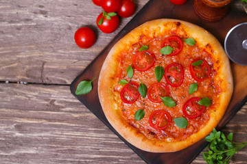 Italian cuisine. Mediterranean cuisine. Pizza Margherita with tomato topped with melted golden cheese, herbs and basil served  on old wooden table