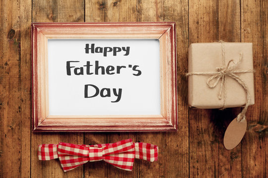 A frame with Happy father's Day greeting, a wrapped box and a plaid bow, on wooden background