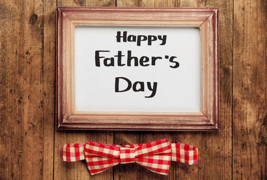 A frame with Happy father's Day greeting and a plaid bow, on wooden background