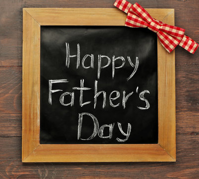 A chalk board with Happy father's Day greeting and a plaid bow, on wooden background