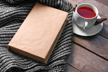 A book, a cup of tea and a woolen blanket on wooden background