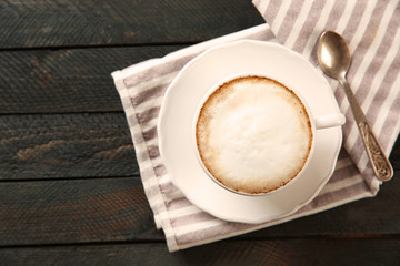 Cup of hot cappuccino with froth and spoon on a black wooden table