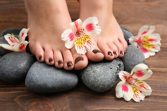 Manicured female feet with flowers on spa stones closeup