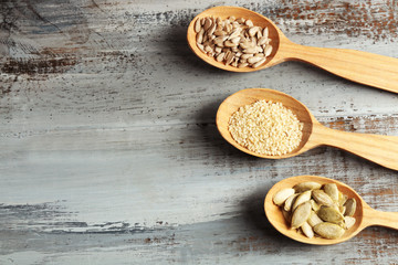 Sesame, pumpkin and sunflower seeds in wooden spoons on blue background, closeup