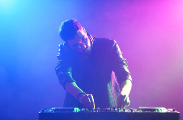DJ playing music at mixer on colorful foggy background
