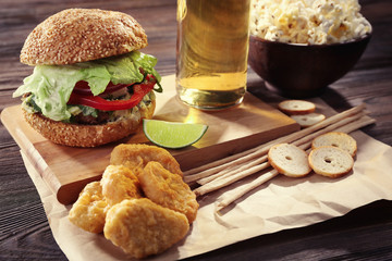 Big tasty hamburger with snacks and glass bottle of light beer on wooden table