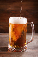 Glass mug of draft light beer on wooden table, close up