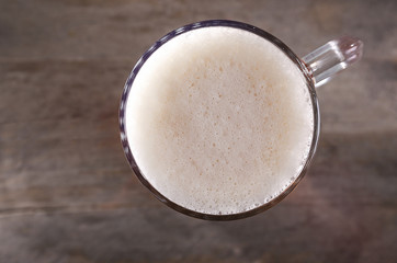 Top view of glass mug of light beer with foam on wooden table, close up
