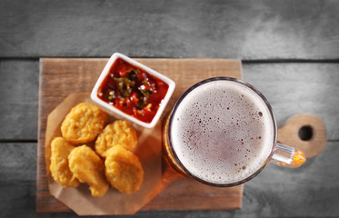 Glass mug of light beer with snacks on wooden table, close up