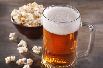 Glass mug of light beer with popcorn on wooden table, close up