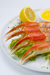 Boiled crab claws with sauce and lemon on a plate over white background
