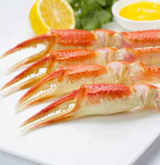 Boiled crab claws with sauce and lemon on a plate over white background