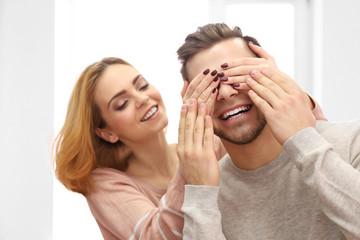 Young woman closing her boyfriend's eyes beside the window
