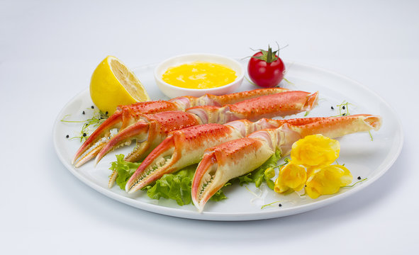 Boiled crab claws with sauce and lemon on a plate over white background