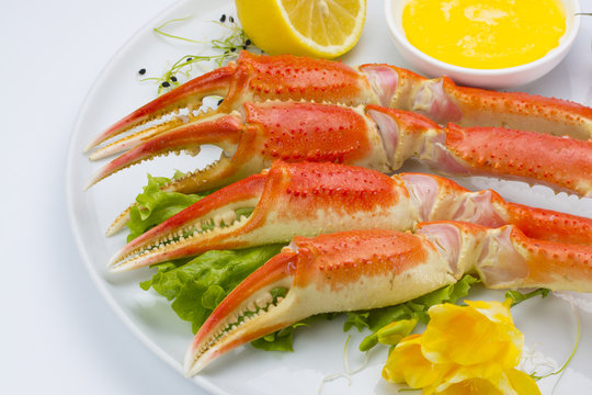Boiled crab claws with sauce and lemon on a plate over white background