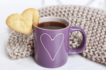 Heart shape cookie on cup of coffee with knitted cloth closeup