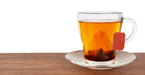 Glass cup with tea bag on wooden table over white background