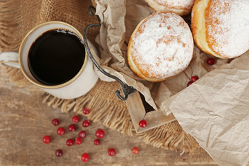 Delicious sugary donuts with red currant on wooden tray with parchment closeup
