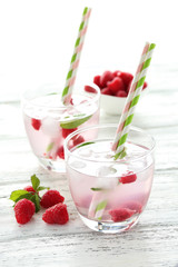 Raspberries and juice in glass on white wooden background