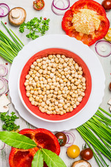 Hummus dish  and various vegetables and seasoning ingredients  for tasty vegetarian cooking on light  rustic wooden background, top view composing. Healthy eating and diet food concept.
