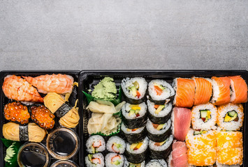 Various sushi menu in black transport box or bento box on gray  stone background, top view, border....