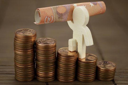 Holzm&auml;nnchen mit Geldschein steigt &uuml;ber eine Treppe aus M&uuml;nzen