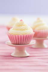Three vanilla cupcakes with buttercream swirl topping on mini cake stands