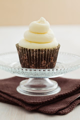 Single vanilla cupcake with buttercream swirl topping on a small cake stand