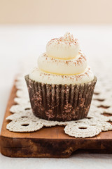 Single vanilla cupcake with buttercream swirl topping and cocoa on a wooden board