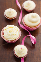 Vanilla cupcakes with buttercream swirl topping with ribbon on wooden table