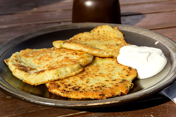 Potato pancakes with sour cream in dark ceramic plate on the wooden table