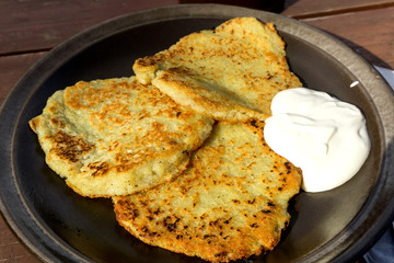 Potato pancakes with sour cream in dark ceramic plate on the wooden table