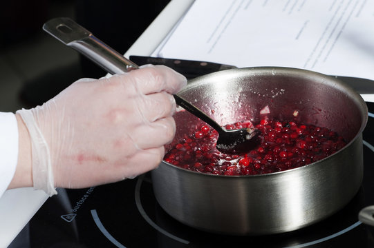 



The cook prepares in the kitchen in a saucepan, cranberry sauce.