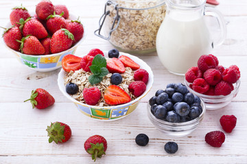 Fresh berries strawberry, raspberries and natural flakes for breakfast, Woman pouring milk into bowl with muesli top view, horizontal