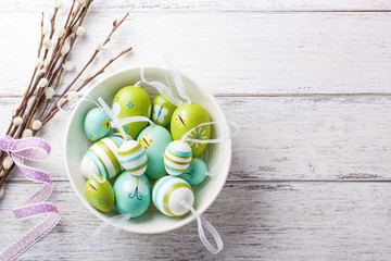 Colorful Easter eggs in a bowl with willow branches and copy space on a wooden background, horizontal, top view..