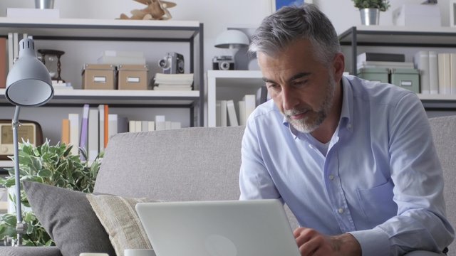 Confident businessman working at home, he is typing on a laptop and checking paperwork