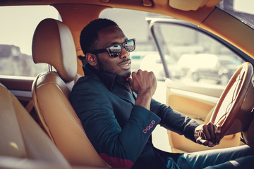 Blackman in sunglasses driving a car.