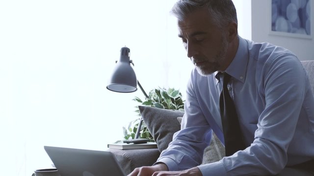 Efficient businessman at home sitting on the sofa and working with a laptop