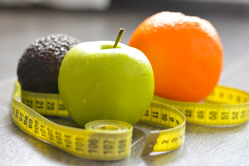Apple, orange and avocado with measuring tape suggesting diet concept