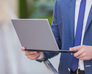 Work in full swing. Successful businessman standing in the street holding a laptop