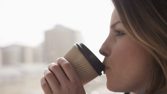 Close up of a woman drinking from a coffee cup whilst sat on a moving train