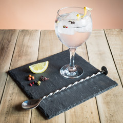 Gin Tonic with botanicals and bar spoon on wood table.