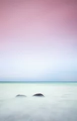 Tuinposter Romantic atmosphere in peaceful morning at sea. Big boulders sticking out from smooth wavy sea. Pink horizon © rdonar