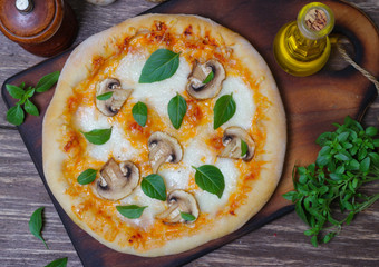 Italian food. Mediterranean cuisine. Delicious pizza with mushrooms and basil - thin pastry crust on wooden background.