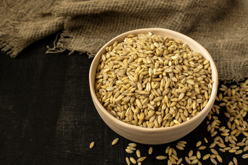 Clay bowl with uncooked pearl barley on a black background