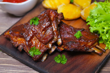 Appetizing rosy and barbecued lamb ribs seasoned with a barbecue sauce and served with fresh herbs and potatoes on an old rustic wooden chopping board